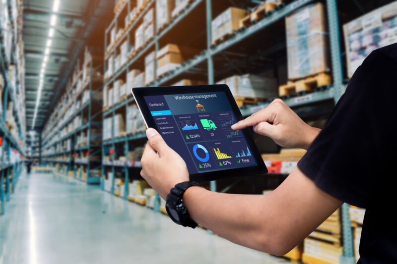Een persoon in een distributiecentrum houdt een tablet vast met een logistiekoverzicht